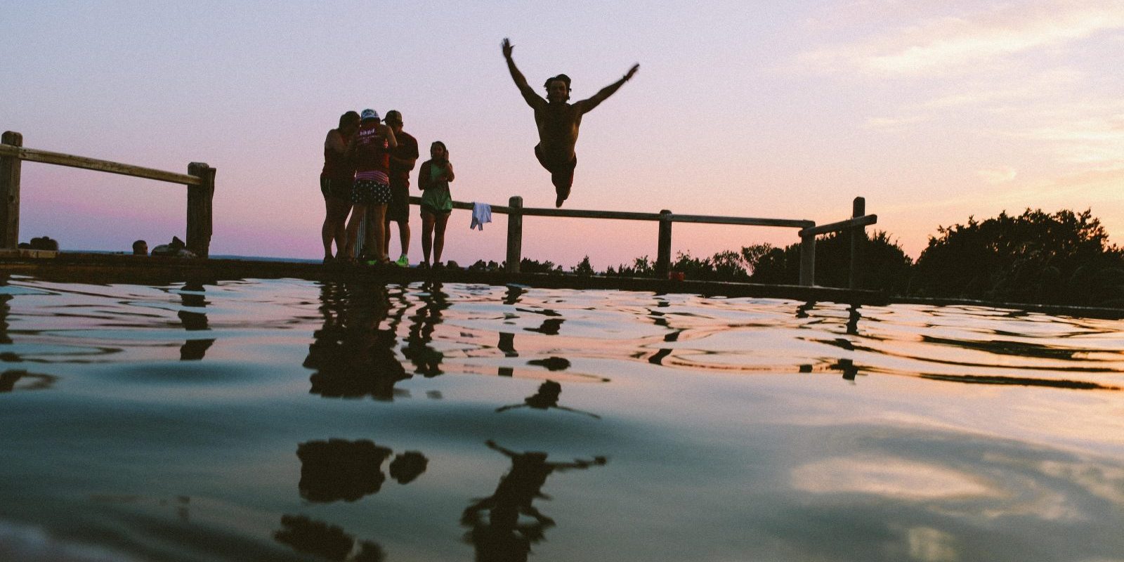 man jumping into the ocean with group of friends