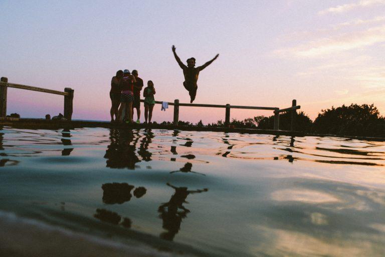 man jumping into the ocean with group of friends