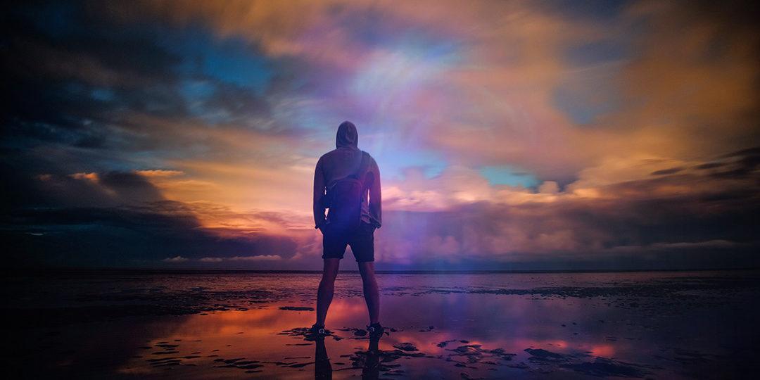 hooded man looking into a sunset at the beach